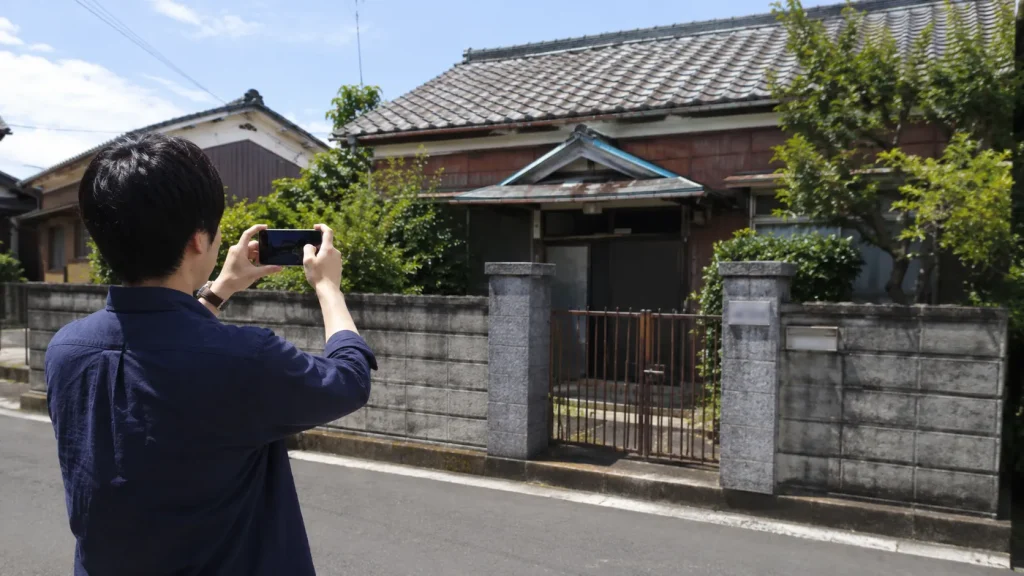 帰省の際に実家の外観をスマートフォンで撮影するイメージ